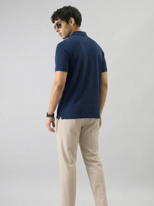 Man wearing a navy blue polo shirt and beige pants on a light gray background