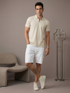 Man wearing a beige polo shirt and white shorts standing in a minimalistic room.
