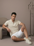 Man sitting on the floor wearing a light-colored polo shirt and white shorts in a neutral setting.